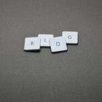 White Scrabble tiles spelling 'Blog' against a minimalist gray background.